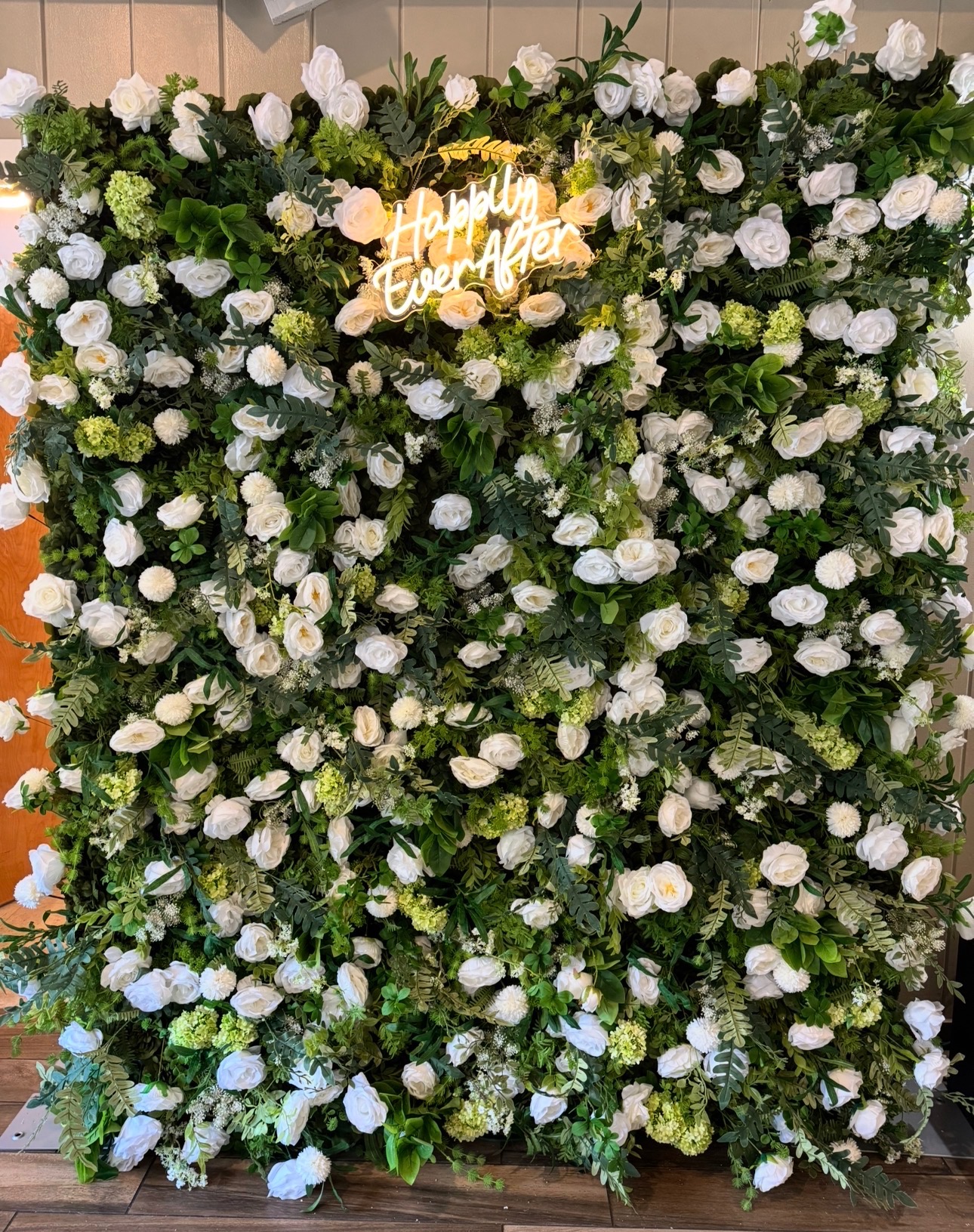 White rose and greenery flower wall with Happily Ever After neon sign