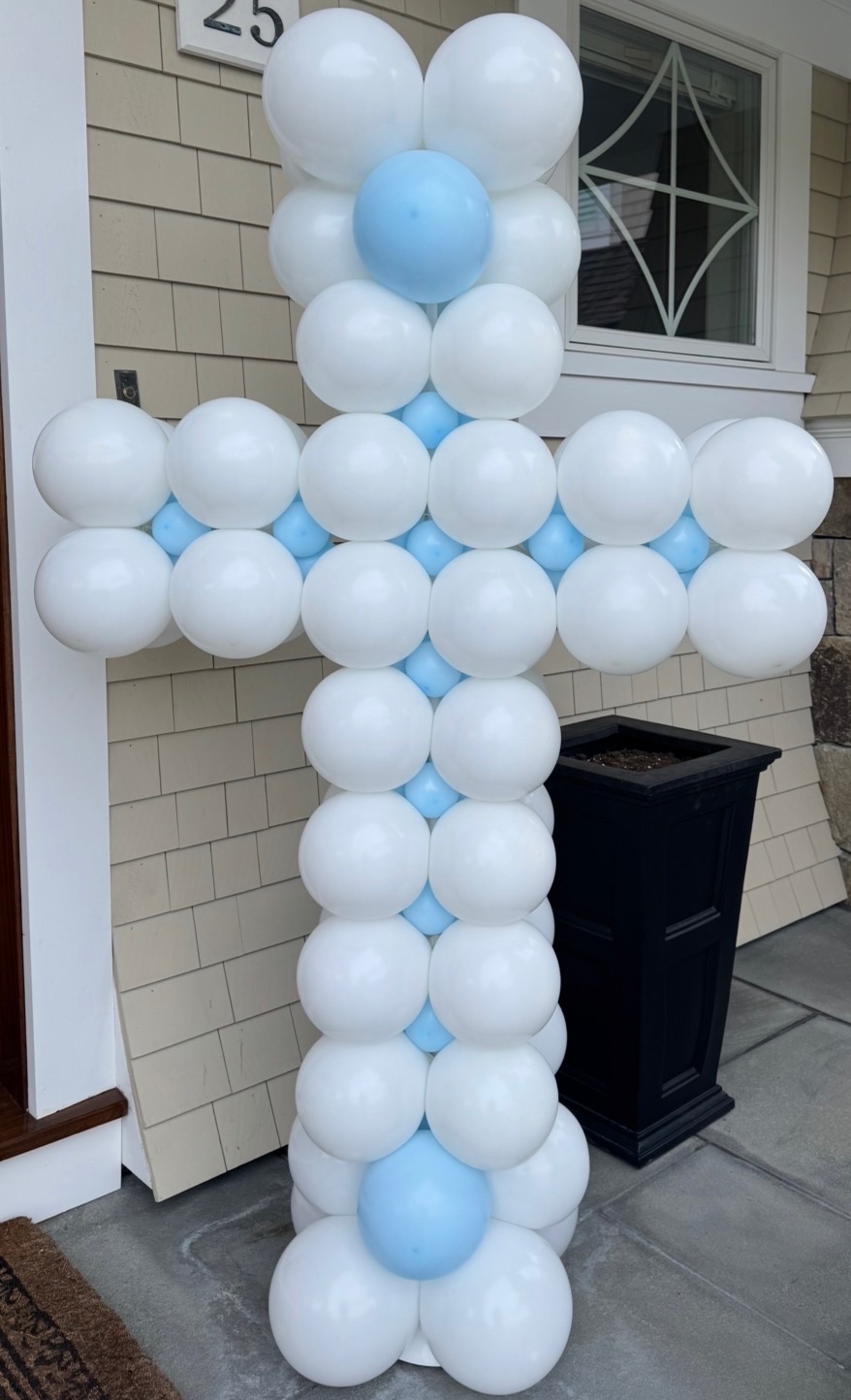 White and light blue balloon cross for a baptism on a front porch